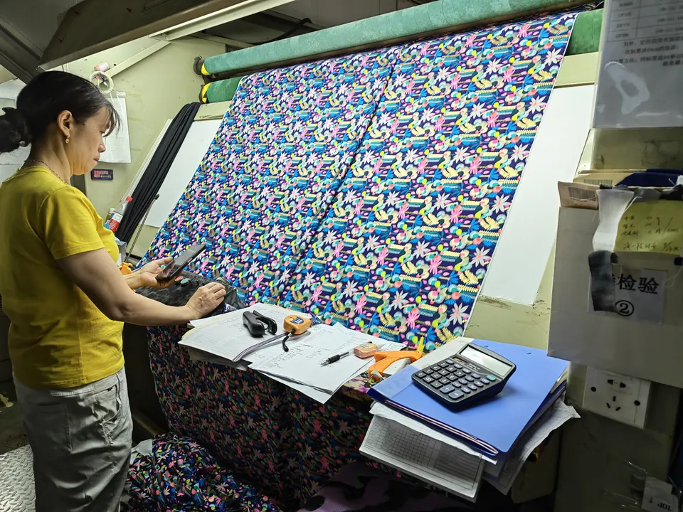 Worker inspecting colorful floral fabric at a textile finishing machine in Keqiao